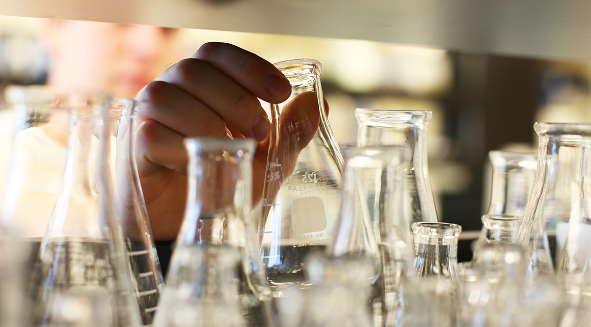A hand reaching for a glass beaker 
